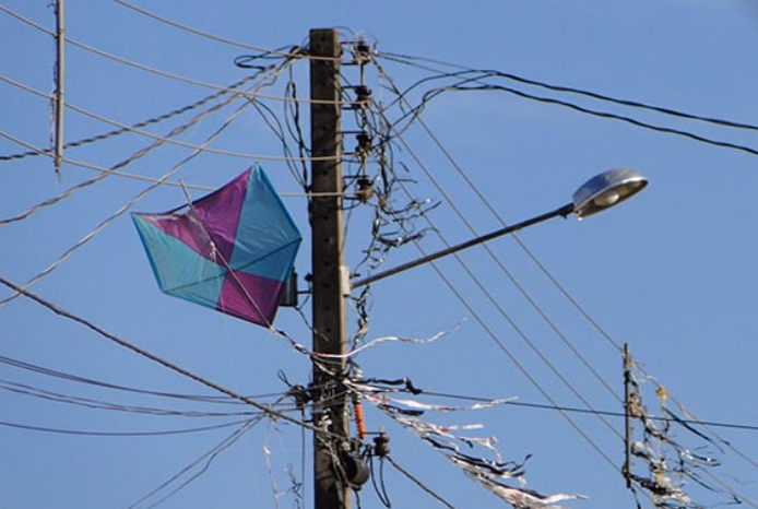 Pipa colorida presa e embaraçada nos fios da rede elétrica, destacando os riscos e perigos dessa brincadeira próxima à infraestrutura energética